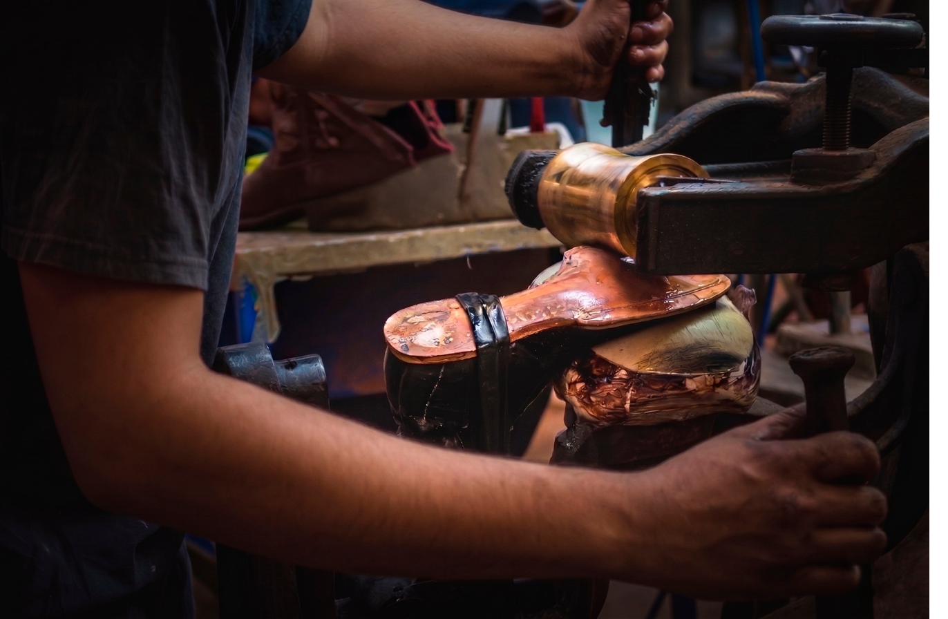 Artisan shaping the heel of a boot under a hand press.